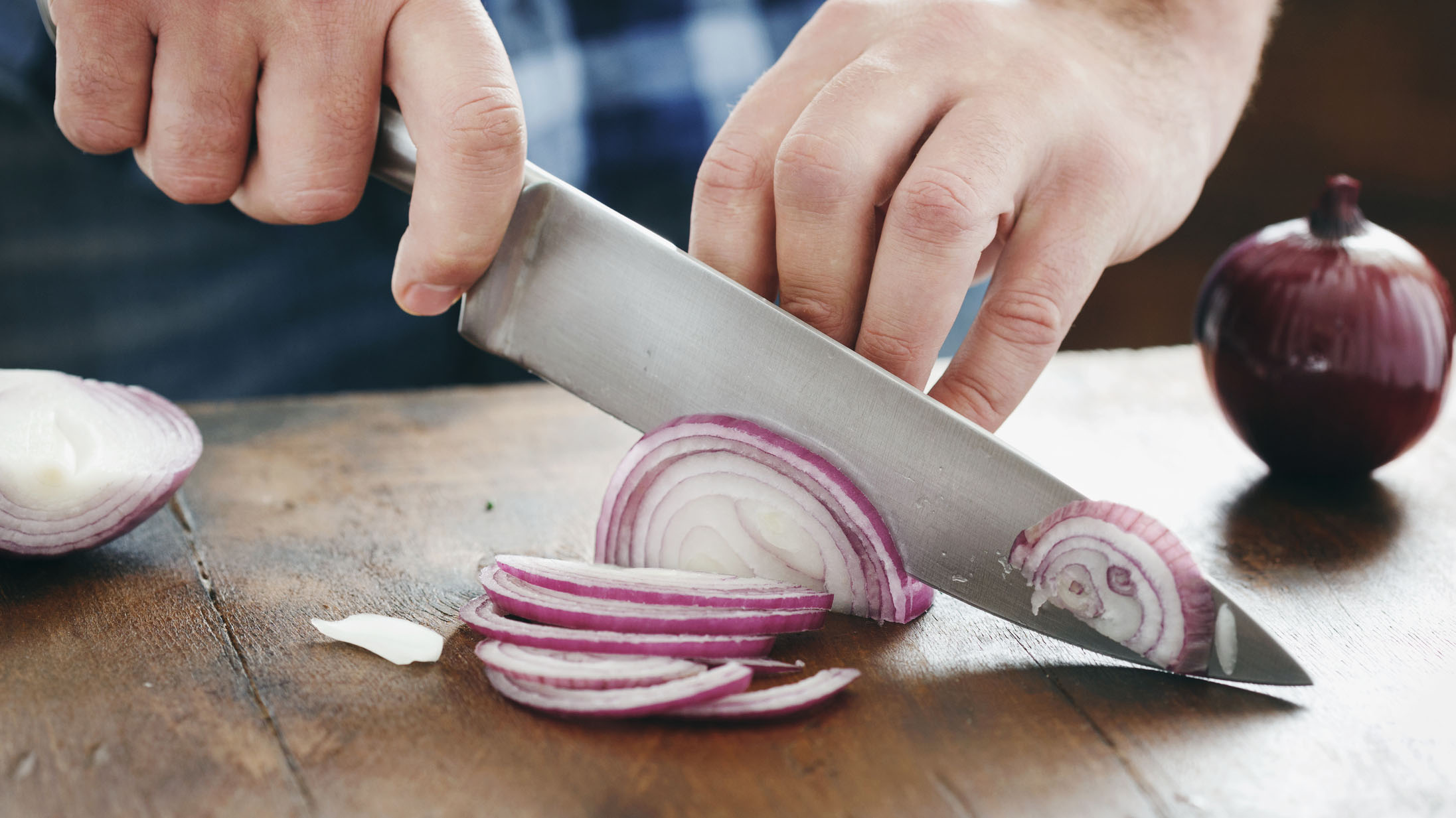 Male hands chopped red onion with a chef's knife on wooden table close up