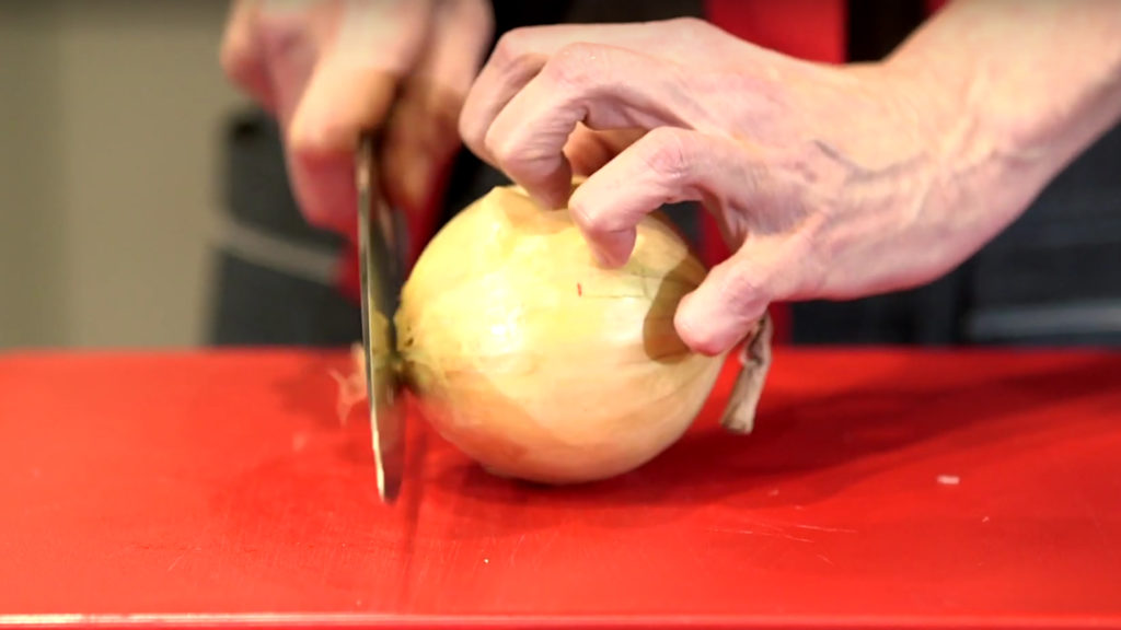 Close up of hand holding a knife and cutting a yellow onion