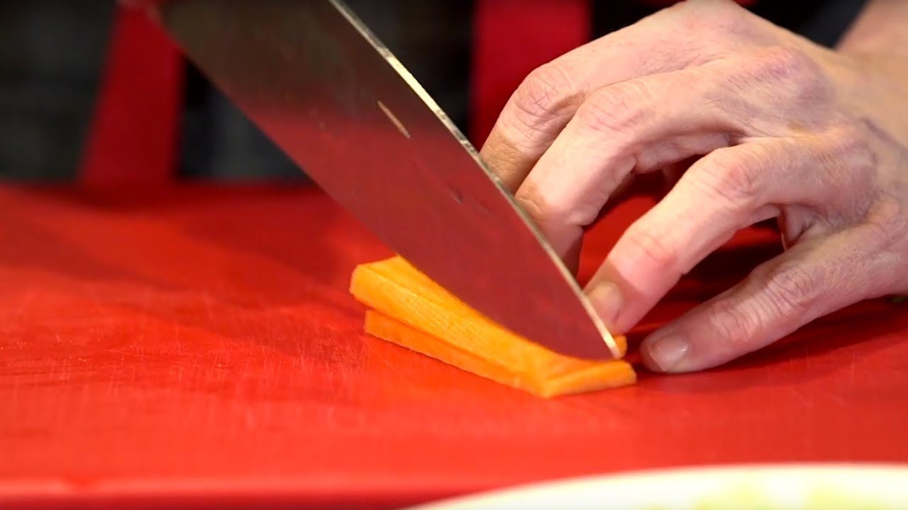 Close up of a hand holding a chef's knife and cutting a carrot