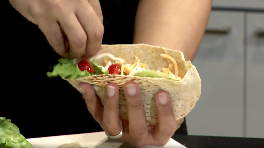 Close up of hands holding a pita pocket with cherry tomatoes, shredded cheese and lettuce as the filling.