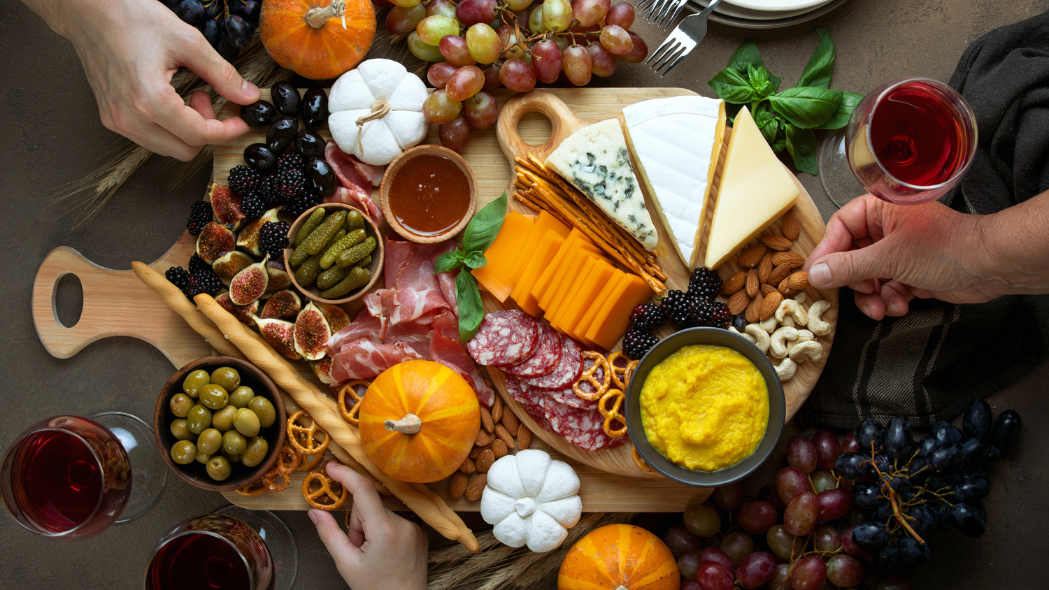 Overhead view of fall holidays table with friends hands picking some fingerfood appetizers from a charcuterie board
