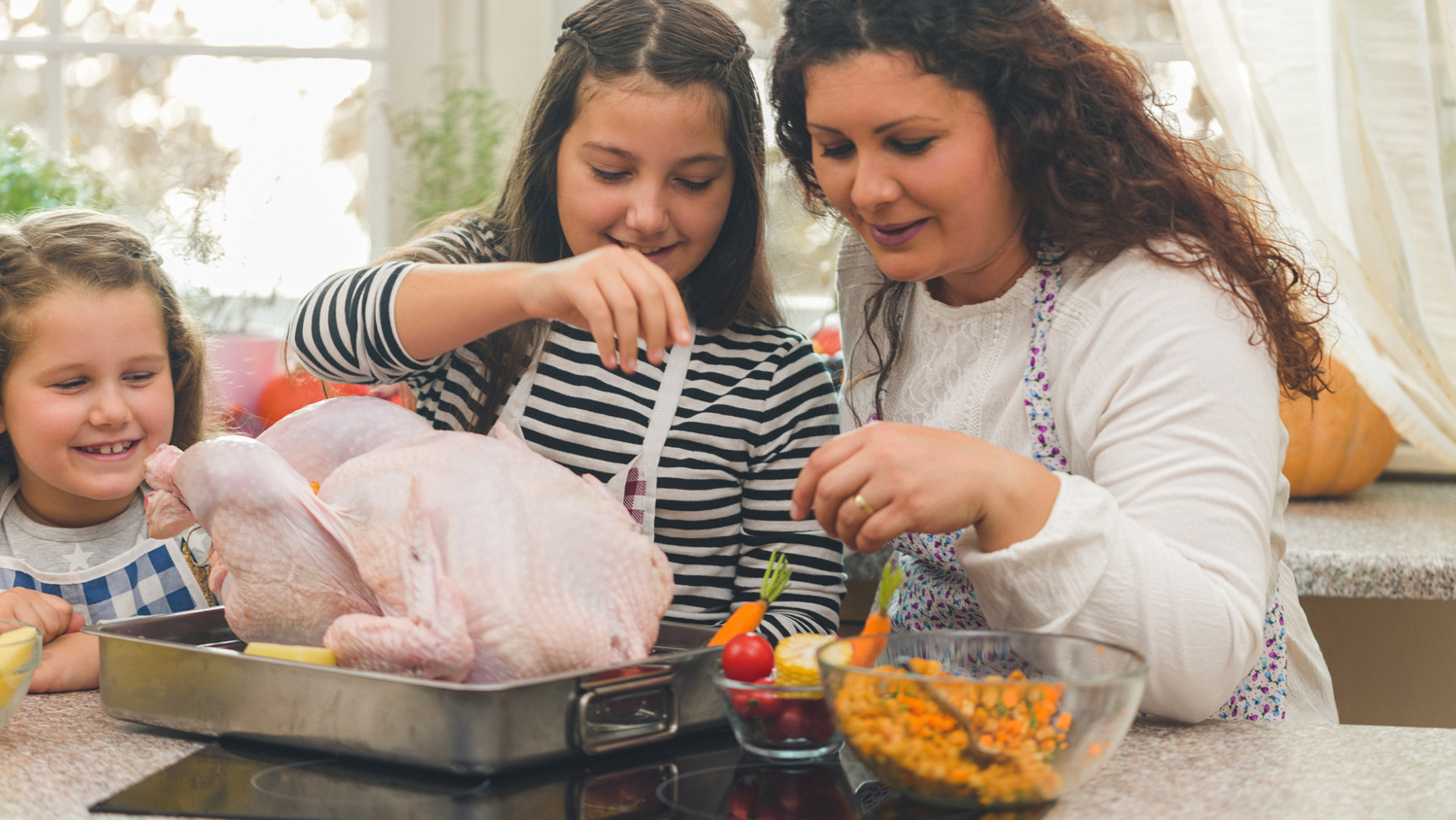Mother and her daughters preparing stuffed turkey with side dishes for Thanksgiving