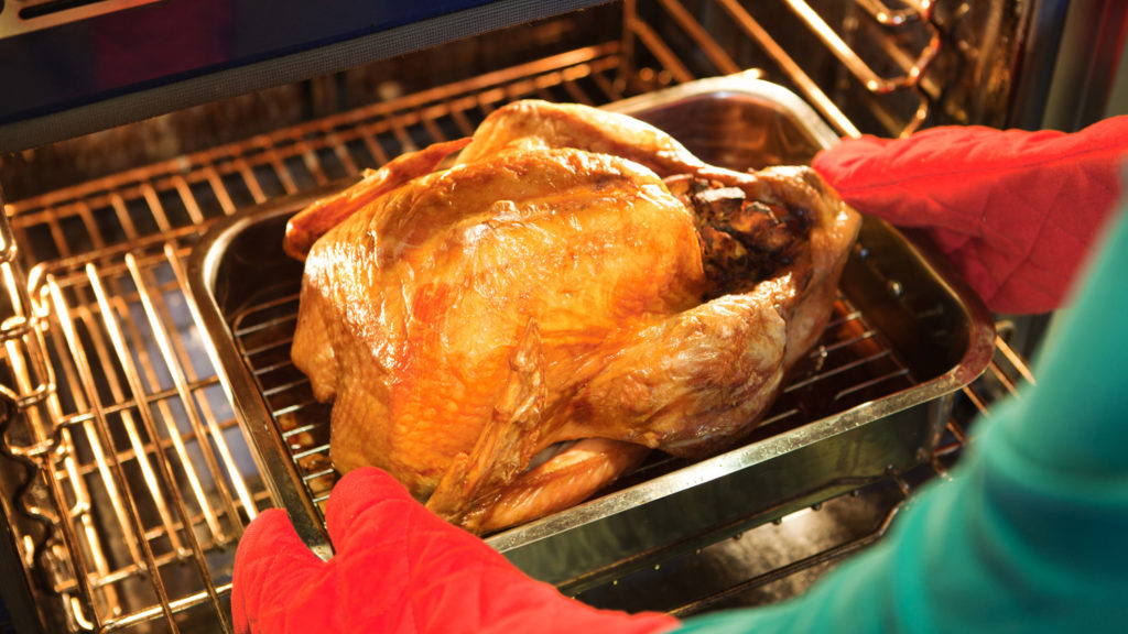 Unidentified person removing a pan of roasted turkey with stuffing fresh from the kitchen oven.