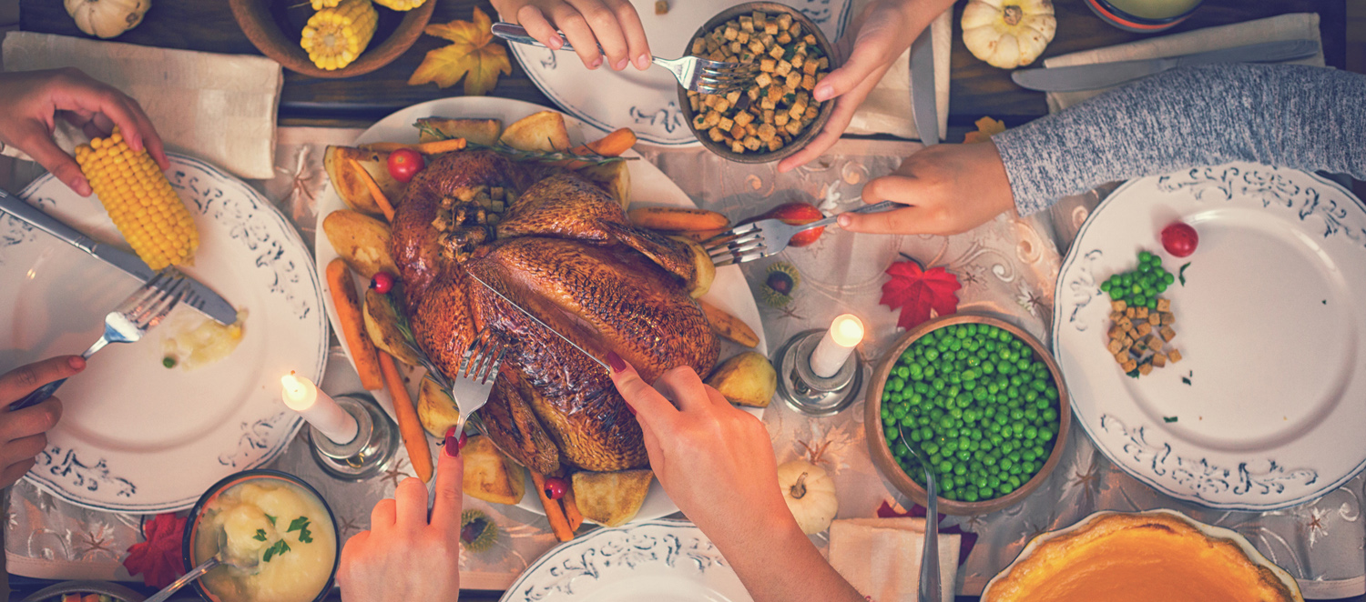 Overhead view of a family celebrating a Thanksgiving or holiday meal at the dinner table with a traditional roasted turkey with side dishes