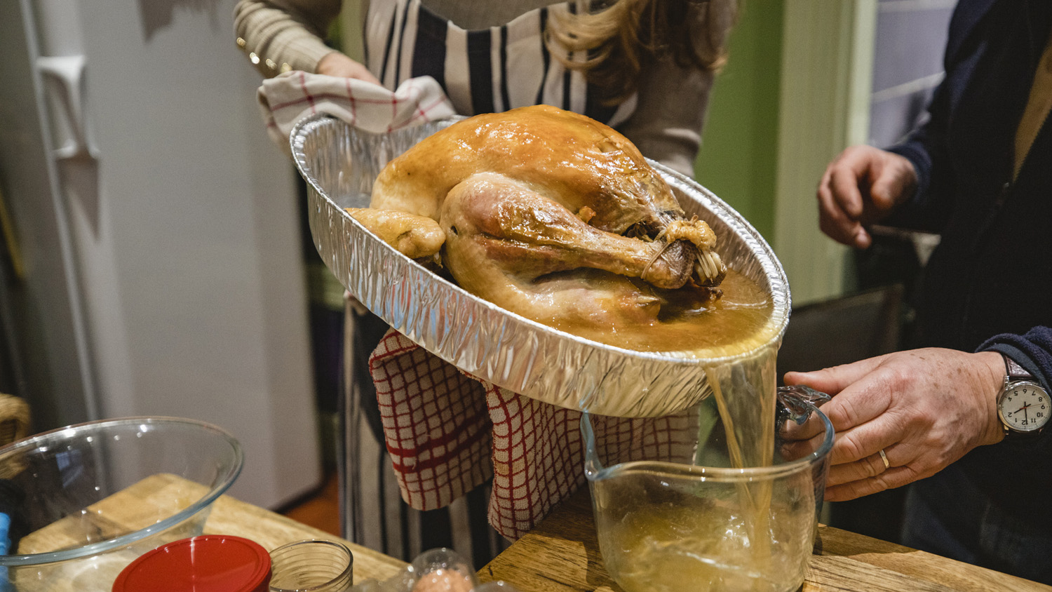 A close-up shot of a woman draining the stock from a roast turkey.
