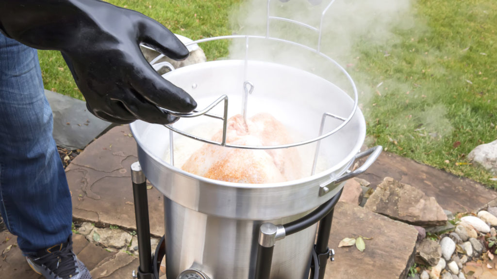Deep fried turkey that has been cooked in a propane gas deep fryer for Thanksgiving is being taken out of the fryer by a man with protective gloves. The fryer is outside because it is too dangerous to have it indoors.