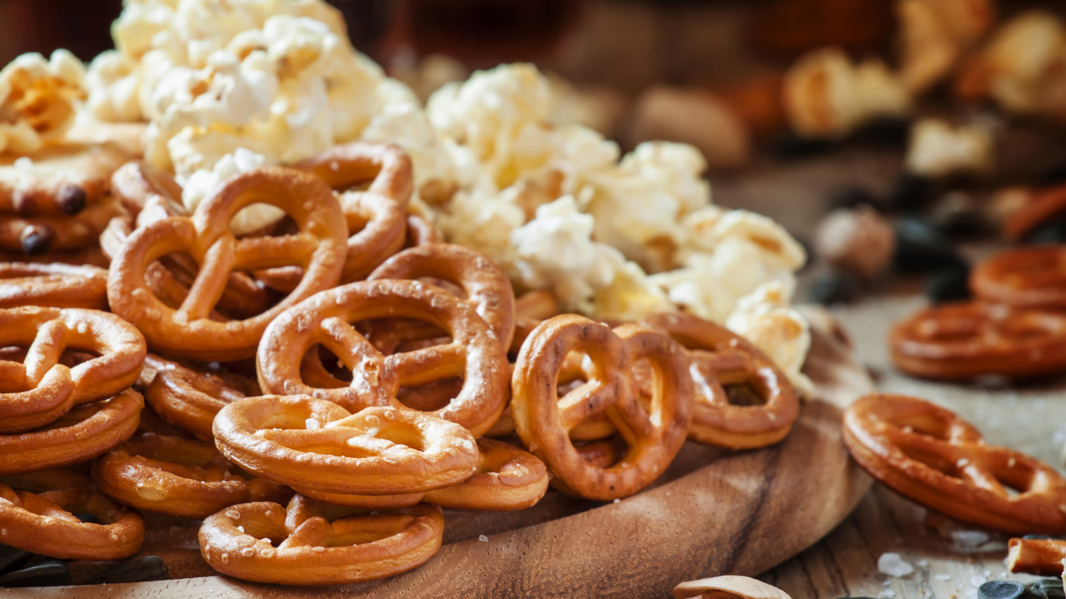 A wooden cutting board with pretzels and popcorn