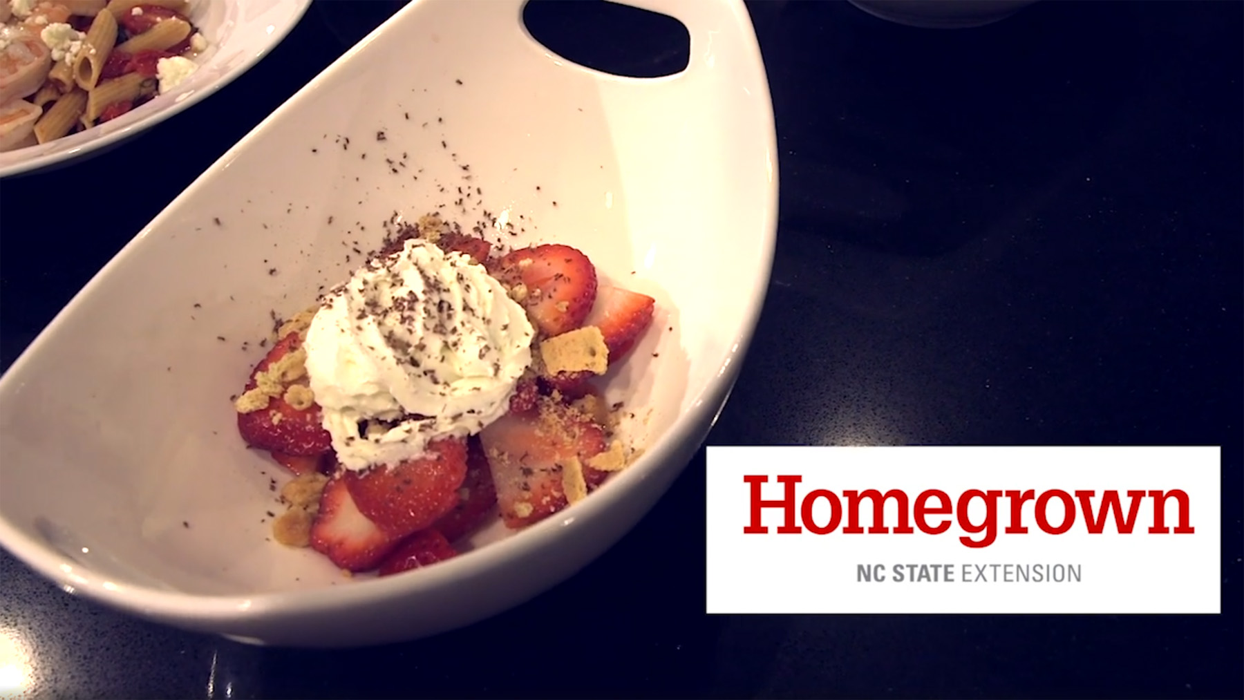 A Grand Marnier strawberry parfait is displayed in a white dish on a black counter with the Homegrown by NC State Extension logo beside it