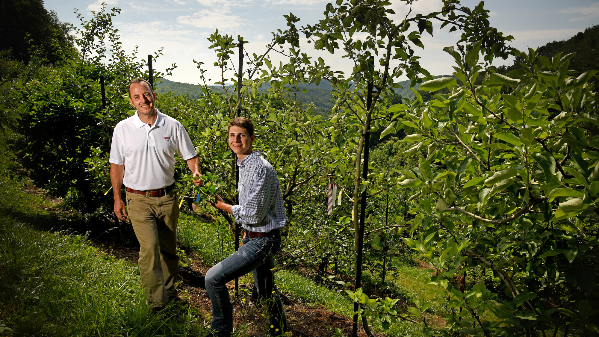 An NC State Extension expert is standing with a student in front of apple trees at an orchard in North Carolina.