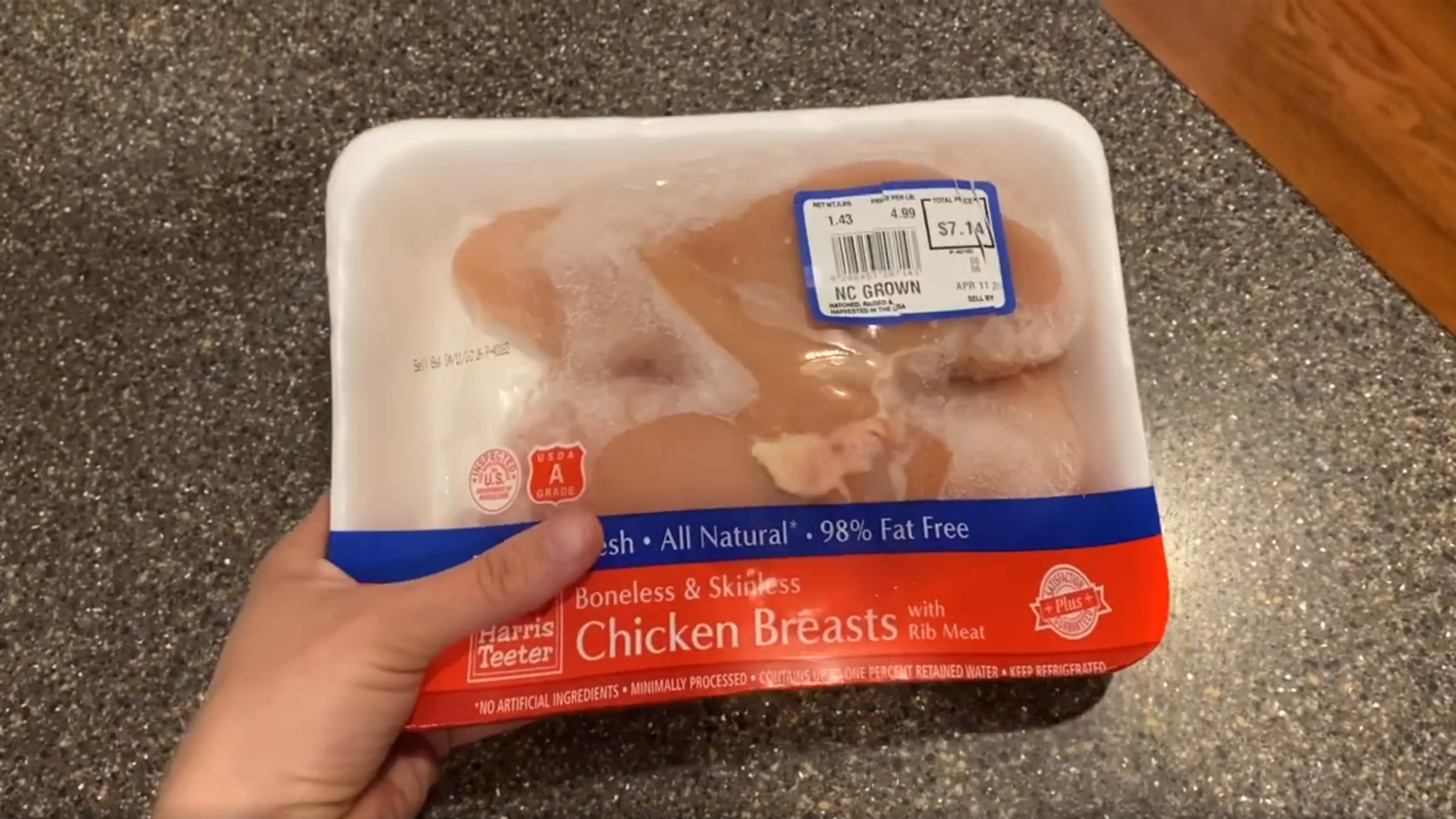 A woman's hand holding a package of frozen chicken.