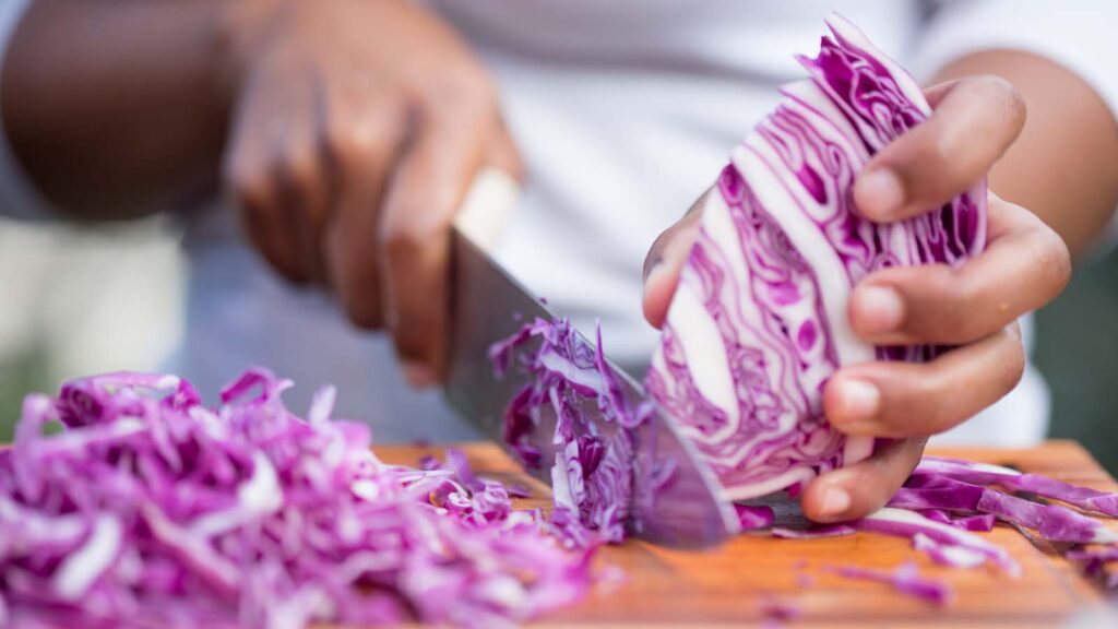 A person chops a head of red cabbage.