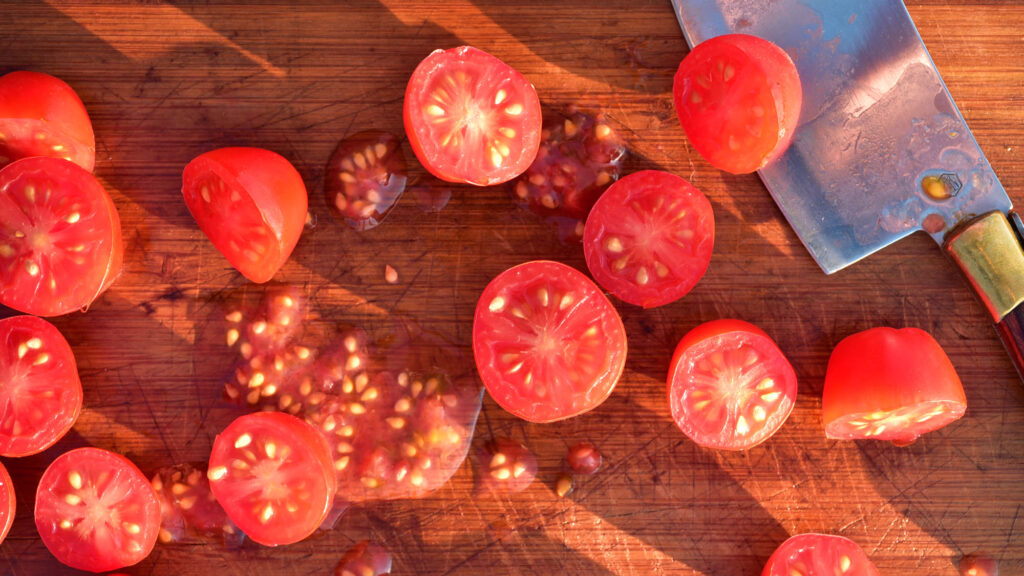 Overhead shot of tomatoes that have been cut in half to show the seeds inside on a cutting board.