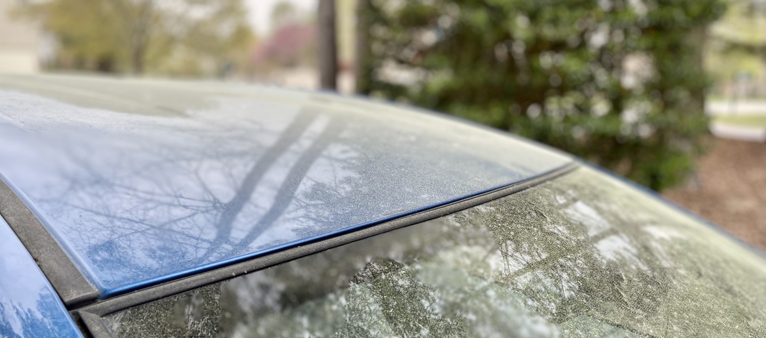 The hood and front window of a blue car is coated with yellow pollen.