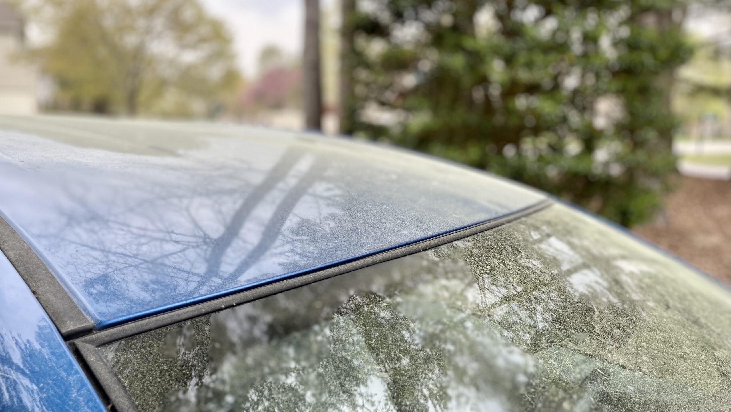 The hood and front window of a blue car is coated with yellow pollen.