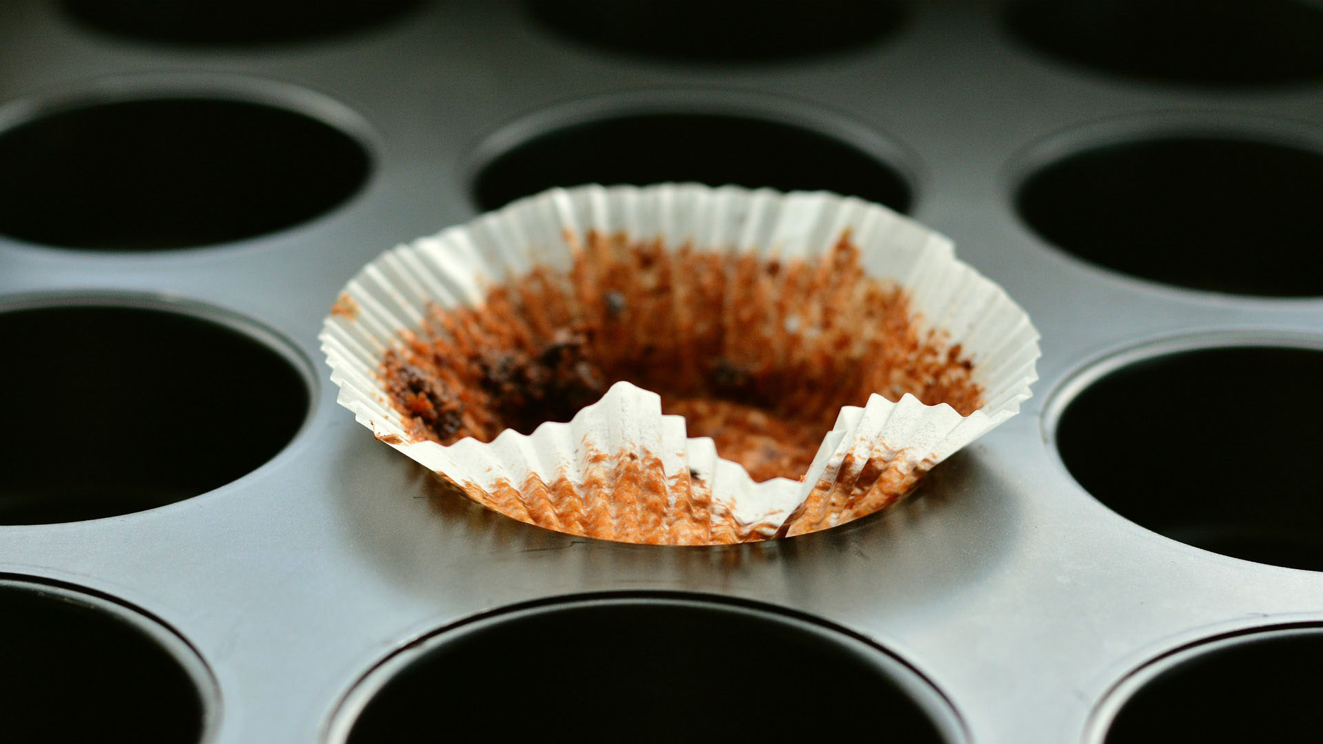 Close-up look at a muffin baking dish with one used paper muffin liner resting crinkled in the center of the dish.