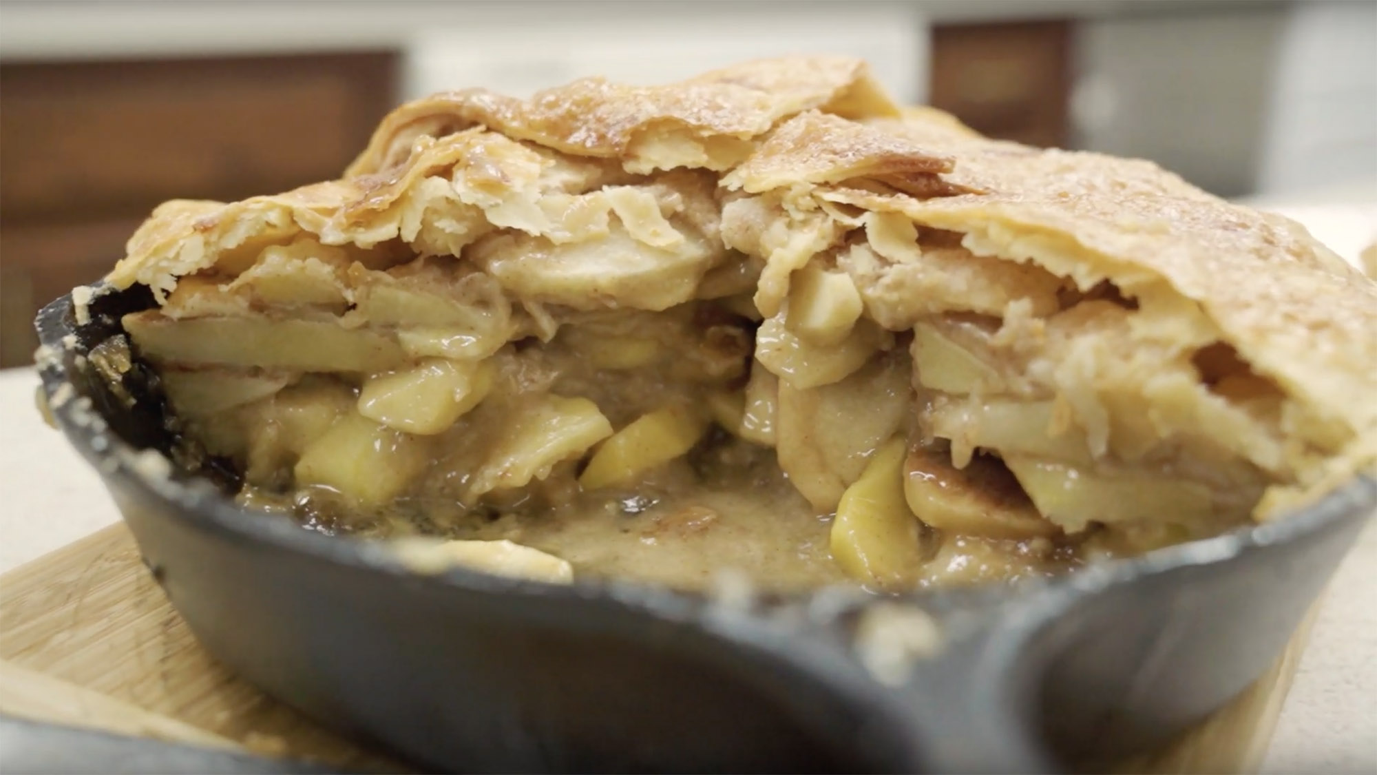A fully-baked mountain high apple pie still in the skillet with a slice cut out showing the apples and ooey gooey goodness inside.