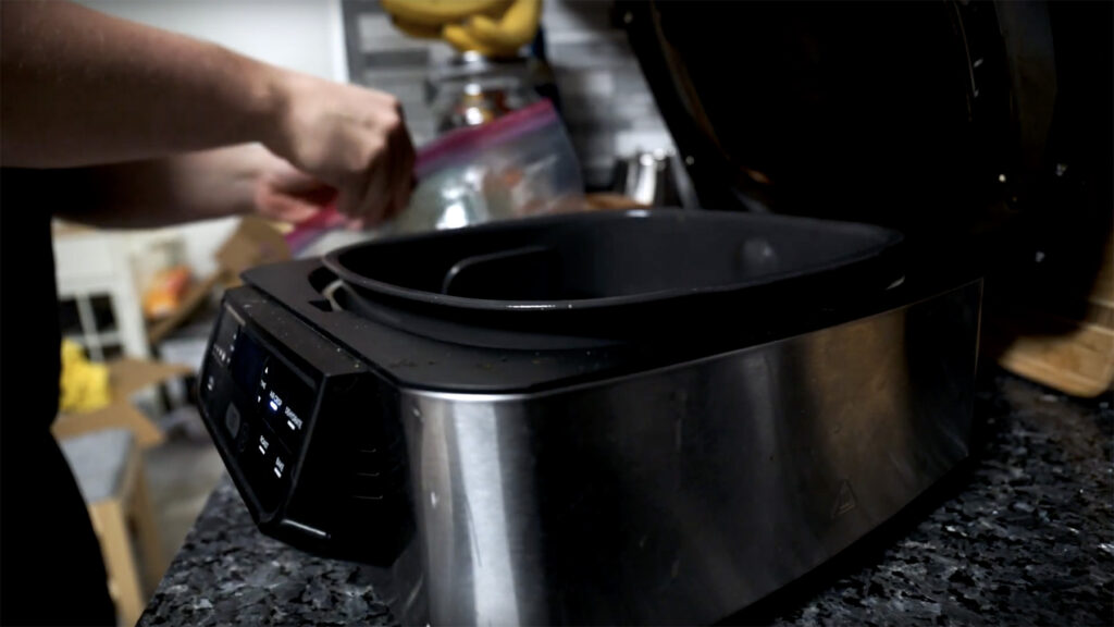 An air fryer on a kitchen counter with someone in the background preparing food to cook.